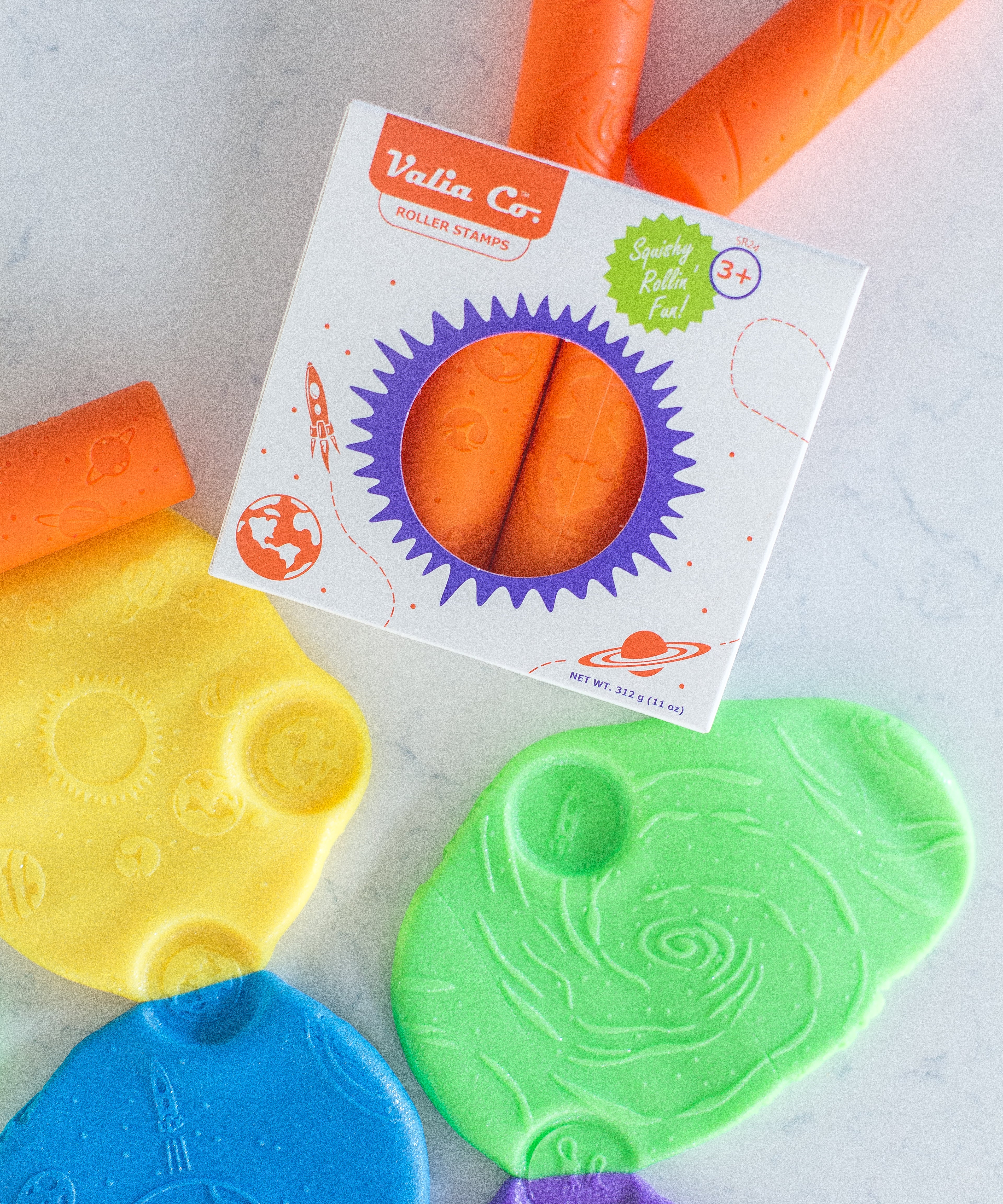 Colorful silicone Valia Co. roller stamps for sensory playdough in box packaging on a light background, surrounded by imprinted playdoh with space exploration designs like STEm galaxy, planets and rockets.
