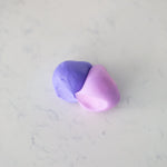 A small piece of clay or dough showing a smooth color transition from purple to pink, resting on a light gray marble surface.