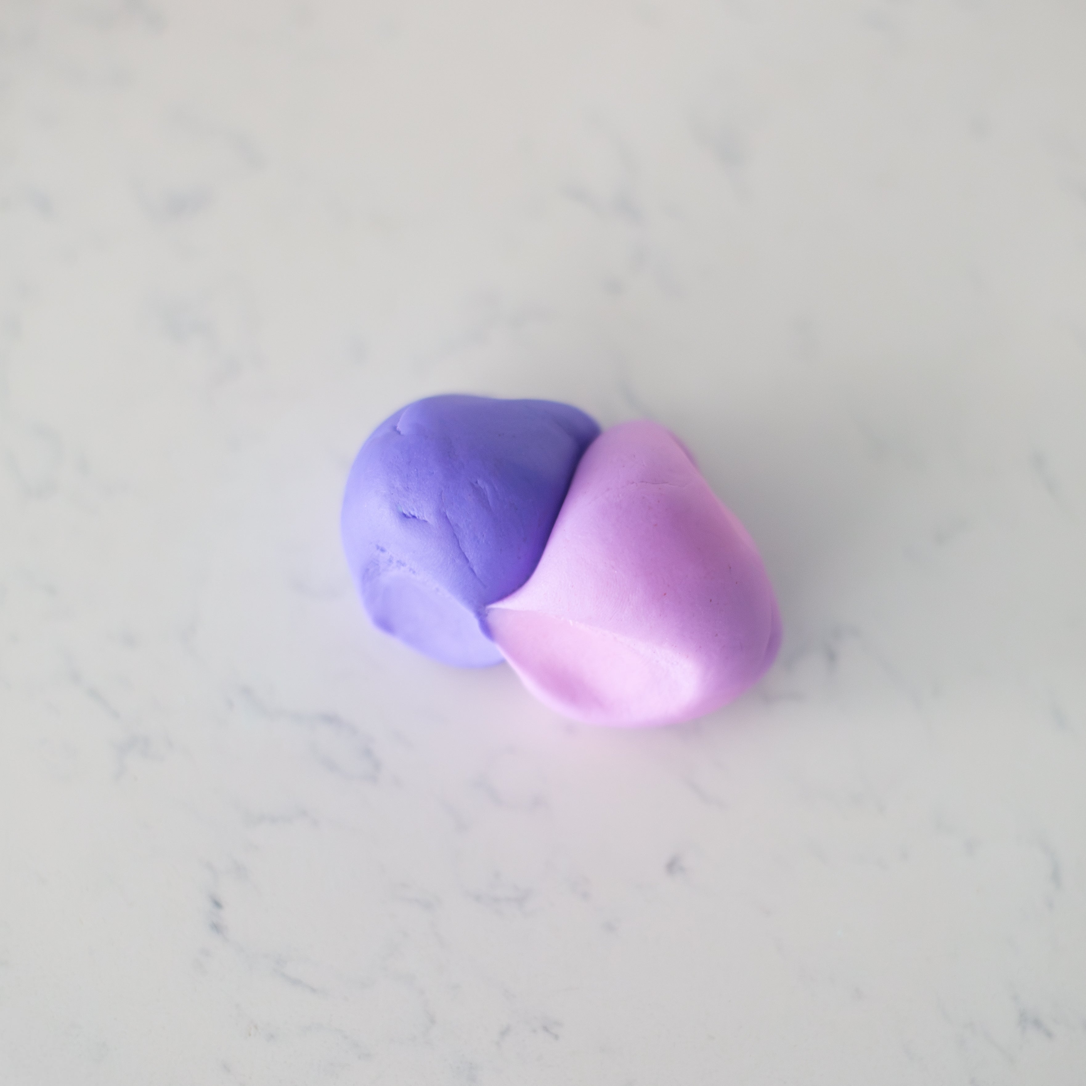 A small piece of clay or dough showing a smooth color transition from purple to pink, resting on a light gray marble surface.
