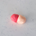 Two small pieces of clay or dough, one pink and one pale peach, resting on a light gray marble surface.