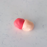 Two small pieces of clay or dough, one pink and one pale peach, resting on a light gray marble surface.