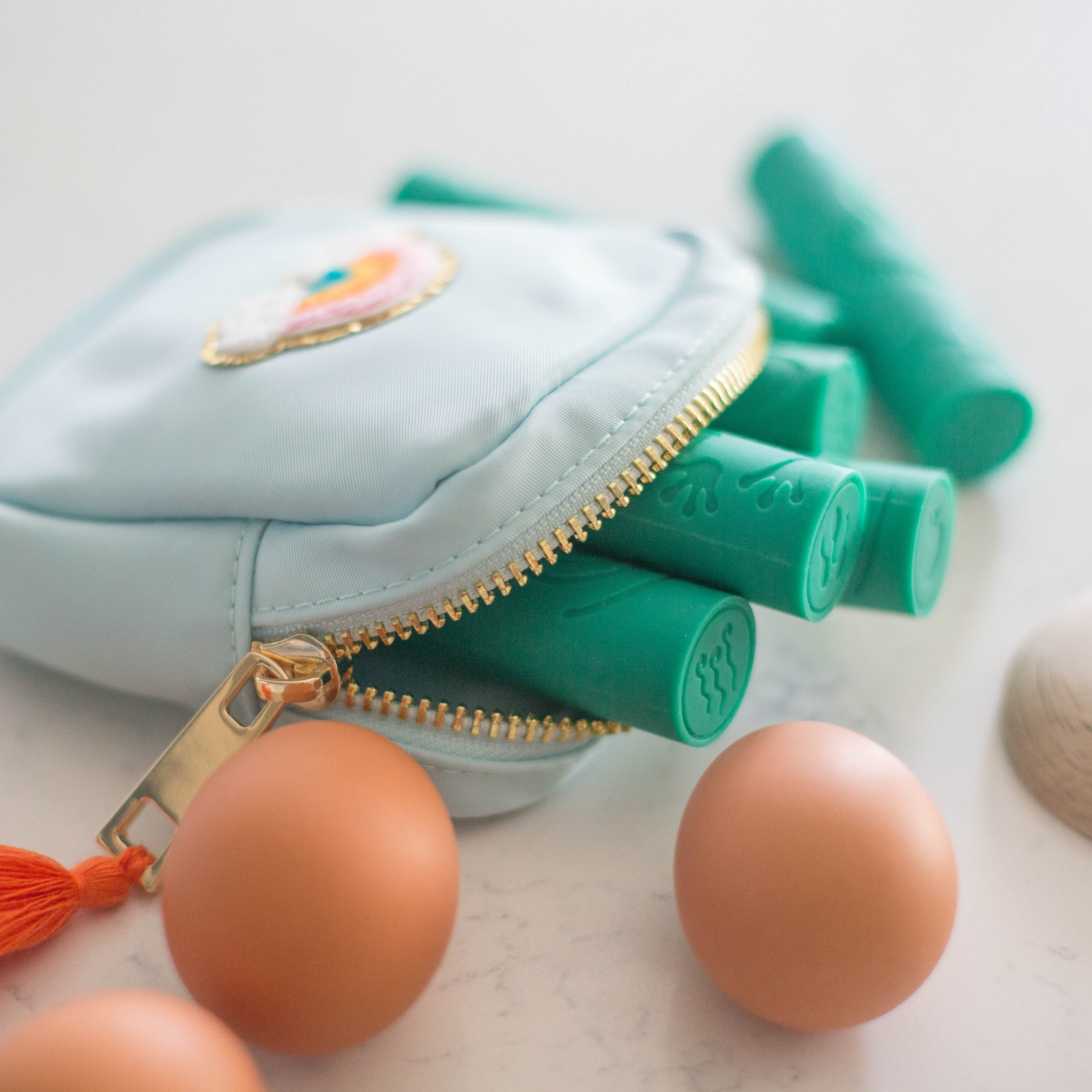 Light blue pouch with gold zipper, green handles, and orange tassel on a white background.