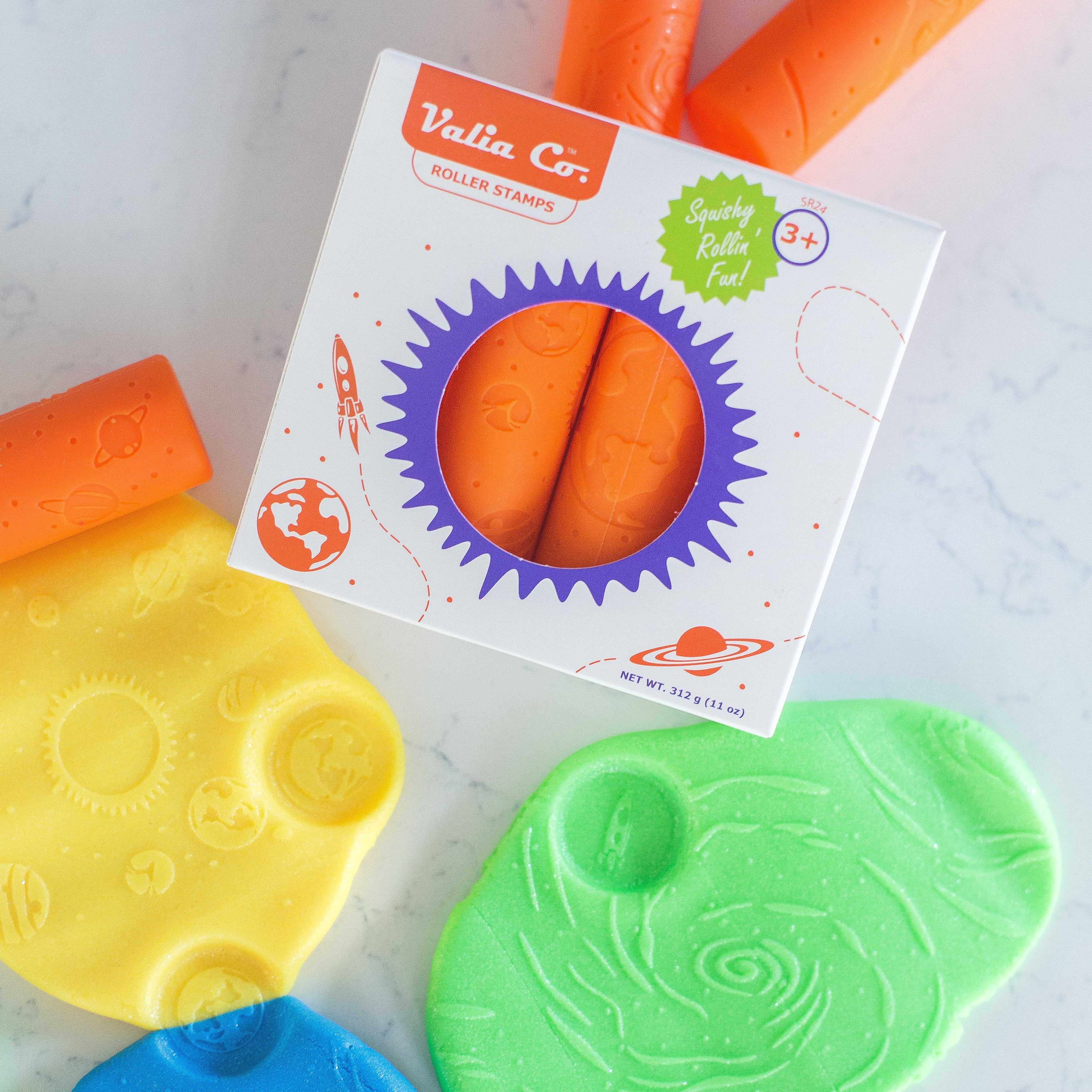 Colorful silicone Valia Co. roller stamps for sensory playdough in box packaging on a light background, surrounded by imprinted playdoh with space exploration designs like STEm galaxy, planets and rockets.