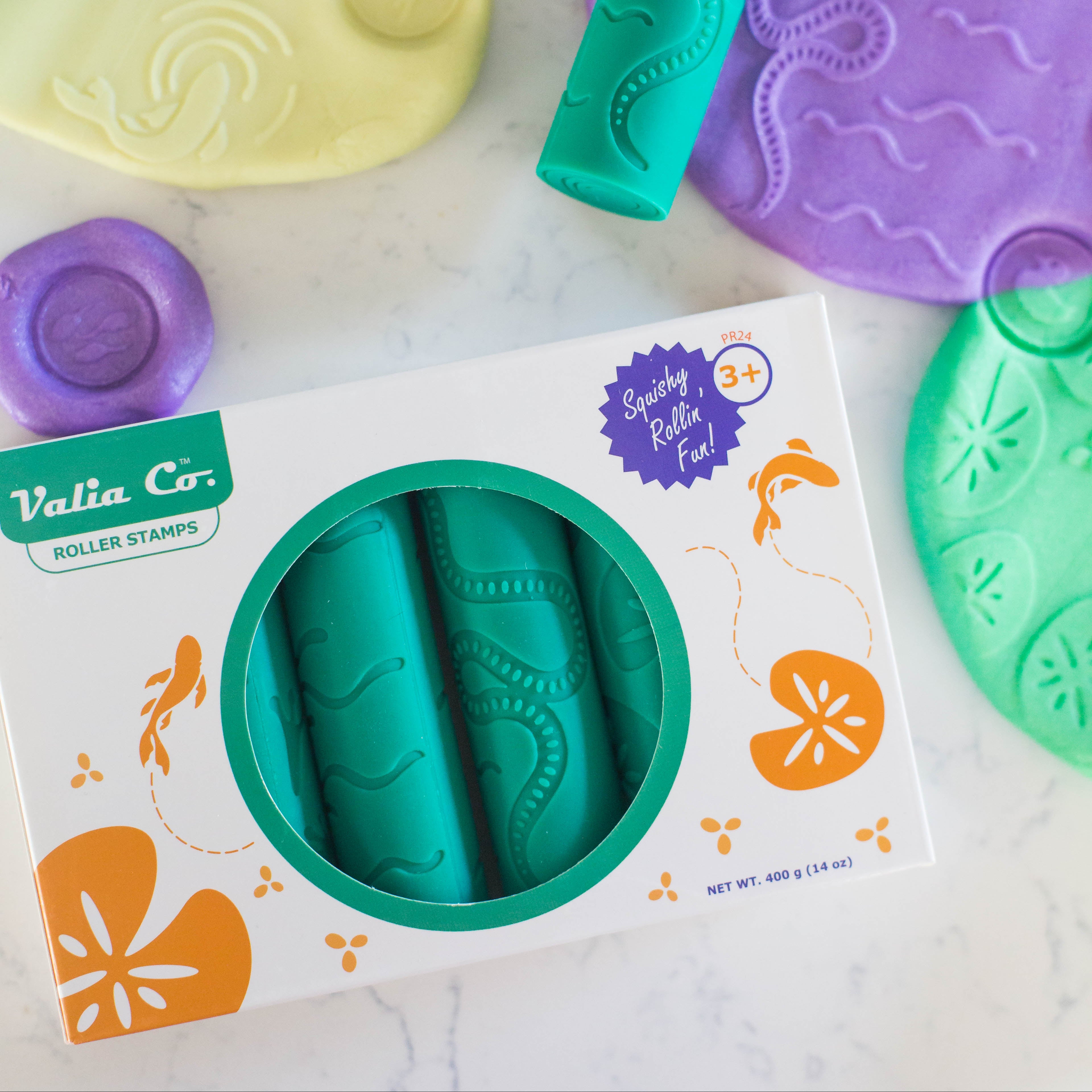 Colorful silicone Valia Co. roller stamps for sensory playdough in box packaging on a light background, surrounded by imprinted playdoh with pond life nature designs like snakes, fish and frog feet. Builds fine motor skills and STEM learning for preschool kids and art crafts.