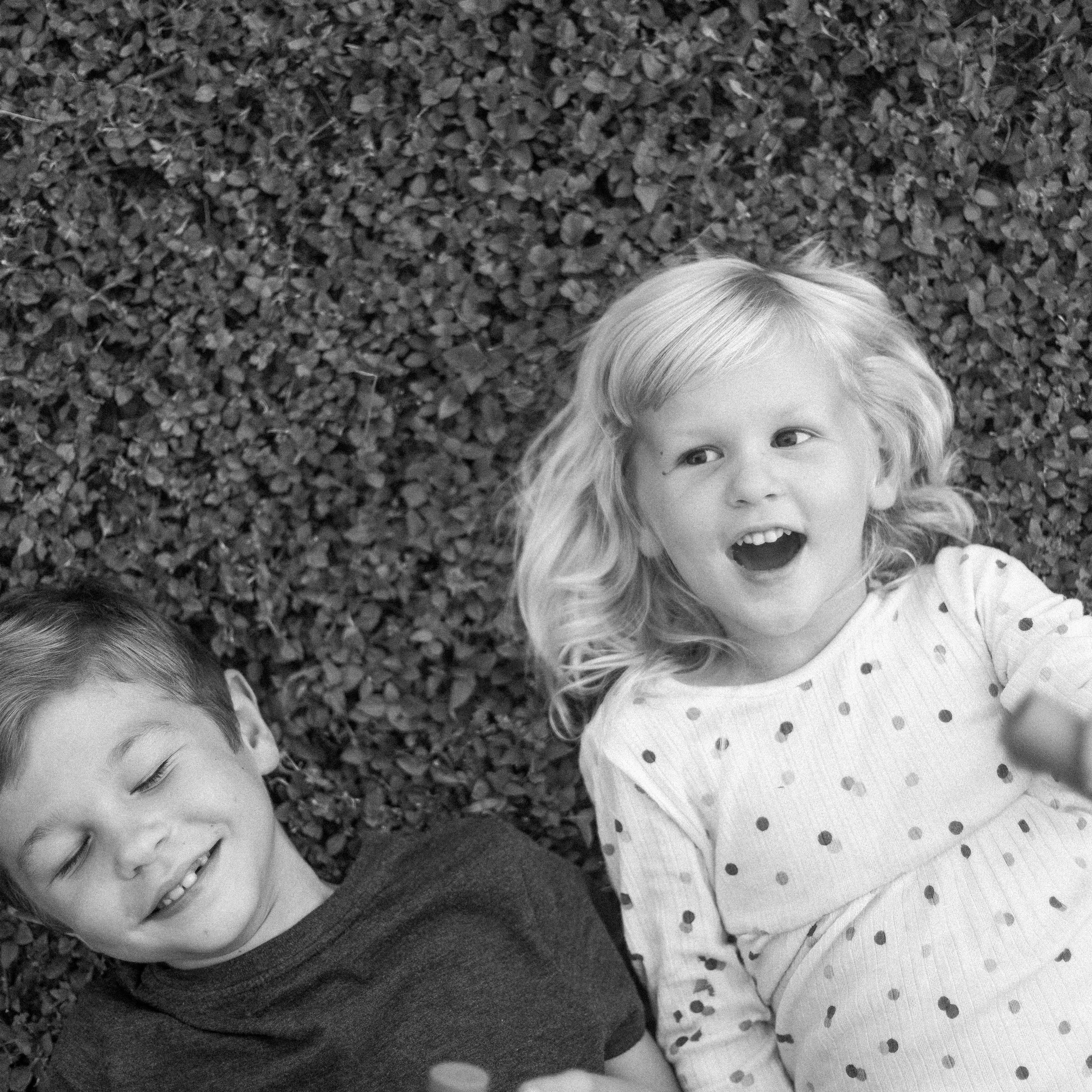 Two children lying on a textured surface, likely grass, in black and white.