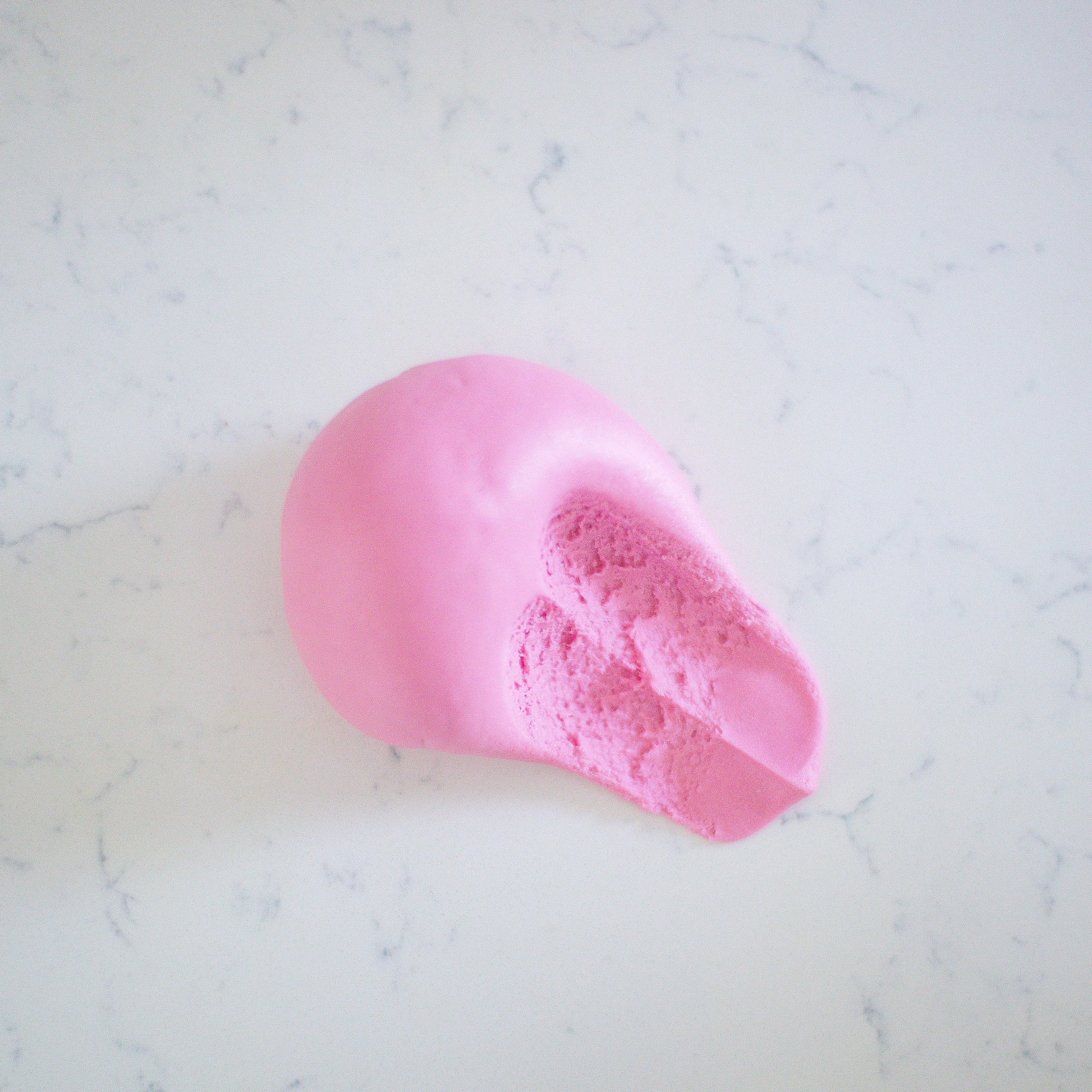A pink ball of smooth play dough, photographed from above on a light gray marble-patterned surface.