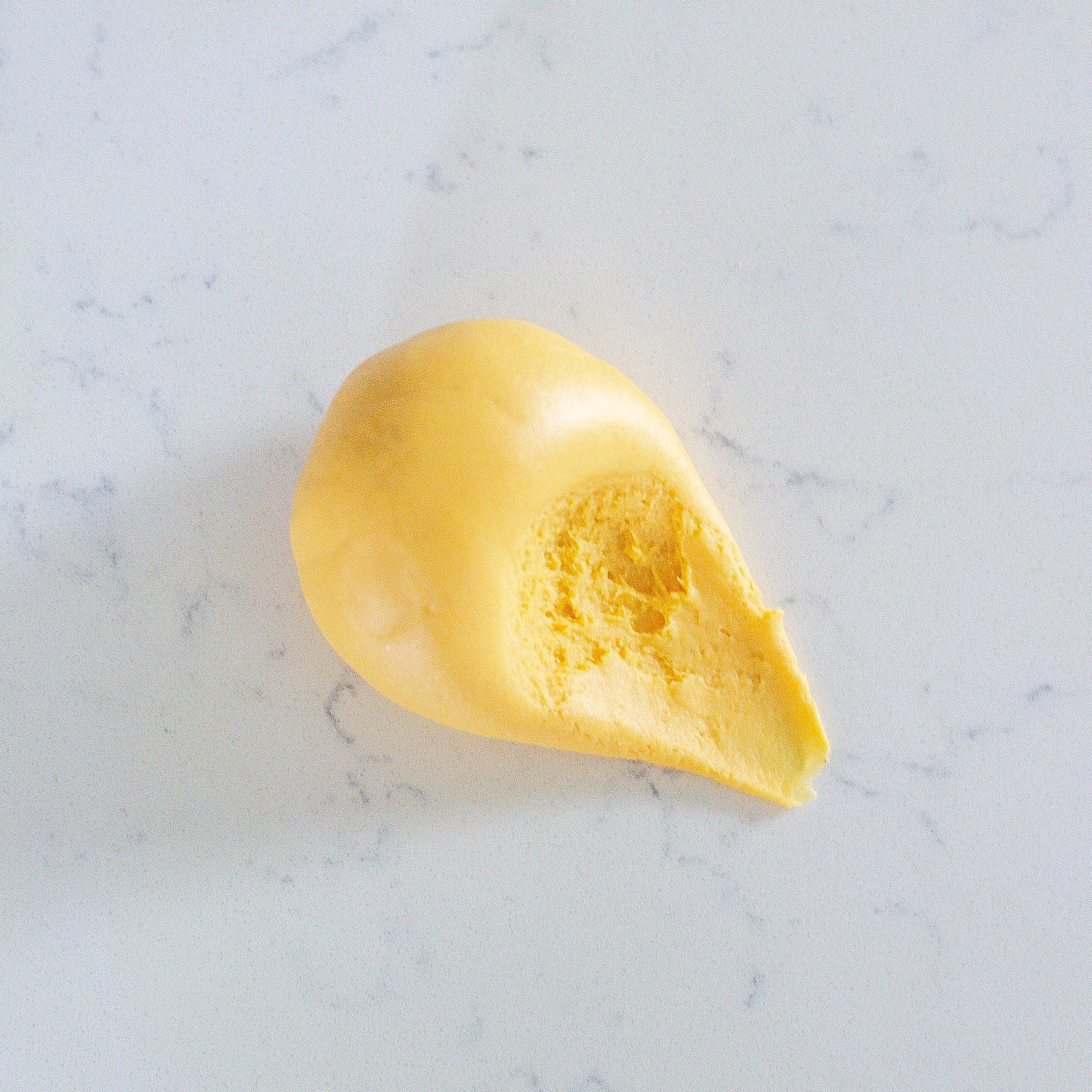 A small dollop of smooth yellow play dough sits on a light marble-like surface.