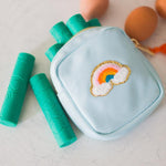 Light blue pouch with rainbow design, green cylindrical items on a light surface